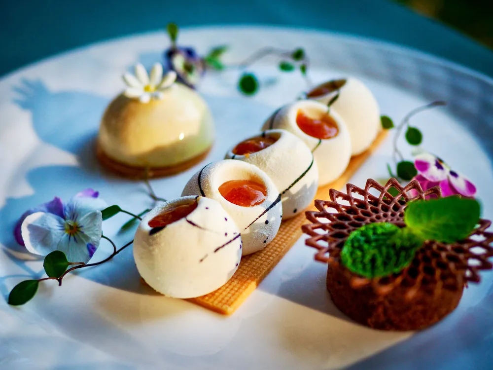 Ein Teller mit kleinen Sahnehauben, Aprikosenkernen, essbaren Blüten und einer Schokoladengittertorte